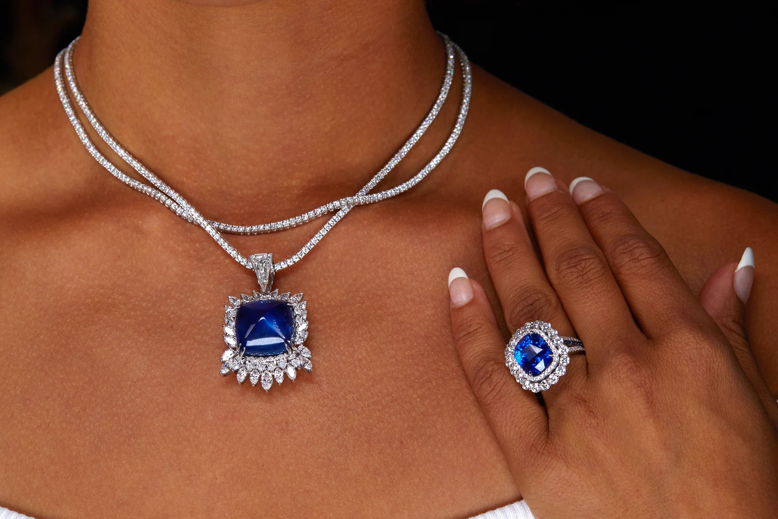 A necklace with a deep-blue gemstone pendant and a coordinating ring, shown being worn